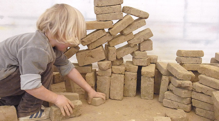 Ein Kind baut mit Lehmsteinen.